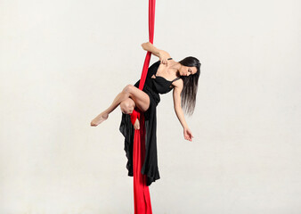Slim young woman performing standing pose on aerial red silks