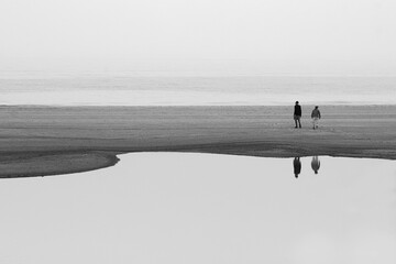 Black and white photo of elderly couple wandering beach with reflection