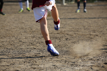 Fototapeta na wymiar kicking a ball on a clay field with boys playing in the background