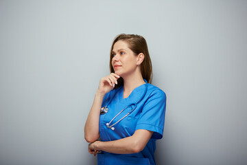 Thinking doctor woman or nurse in blue medical suit looking away.