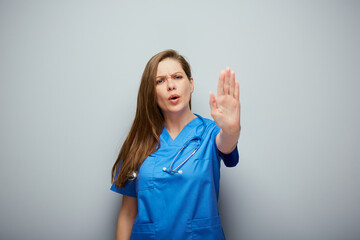 Stop gesture. Doctor woman or nurse in blue medical suit showing palm forward. - 560019360