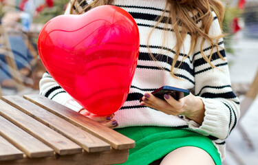 woman sitting in on table with paper hearts garland in one hand using smartphone with another,girl hugging red balloon heart shape.celebrate love valentine day coffee shop inside transparent balloon
