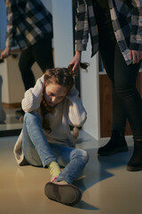 The concept of domestic abuse of a child by mother. Mother pulls the child's hair. Scared little girl, victim sitting on the floor in front of a mirror hiding from her abusive mother.