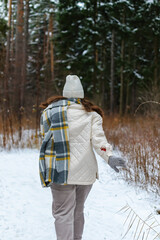 Outdoors view from the back of a young woman in a plaid scarf with warm gloves, running briskly through the snow into the depths of the forest, copy space.