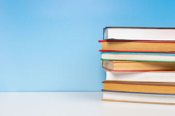 Stack of books in the colored cover lay on the wooden  table and blue backround. Education learning concept