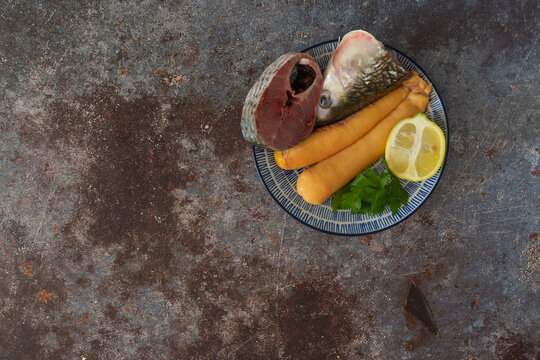 huevas crudas de m&uacute;jol con rodaja y cabeza de pescado sobre un plato azul en fondo de piedra gris y rojo