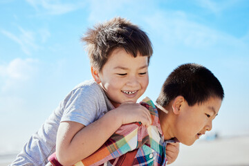 Asian kids, siblings and piggyback on the beach for fun summer vacation together in the outdoors. Happy Japanese children with smile playing by the ocean coast on a back ride on a warm sunny day