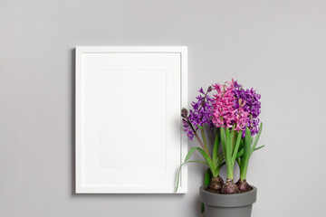 Blank portrait frame mockup on grey wall with hyacinth flowers in pot