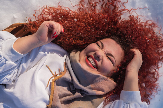 Top view of a fat red-haired woman lying on the snow.