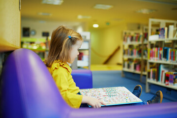 4 year old girl sitting on the floor in municipal library and reading a book
