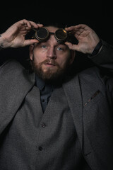 Obraz premium charismatic man in a classic suit and steampunk goggles on a black background stylish Portrait