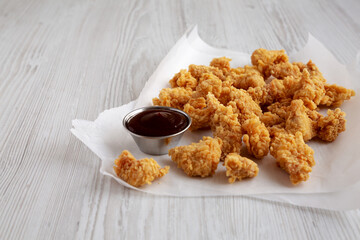 Homemade Popcorn Chicken with BBQ Sauce on a white wooden background, side view.