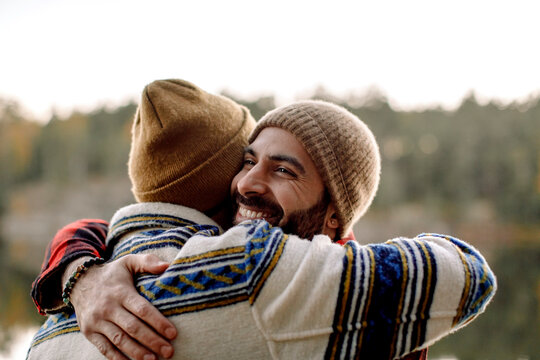 Happy Male Friends Embracing Each Other Wearing Knit Hats