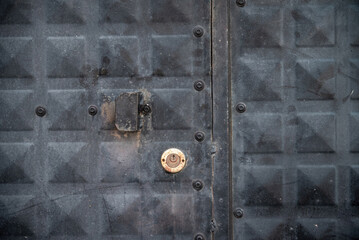 Front view of weathered black iron door with keyhole and lock