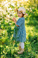 a little girl in a hat by a flowering tree in a spring garden