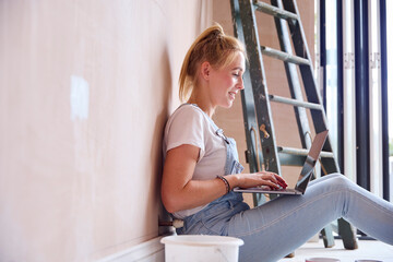 Woman Renovating Kitchen At Home Sits On Floor With Laptop Taking A Break From Decorating Kitchen