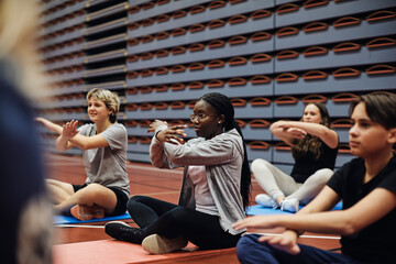 Teenage girls and boy gesturing while practicing yoga in sports court