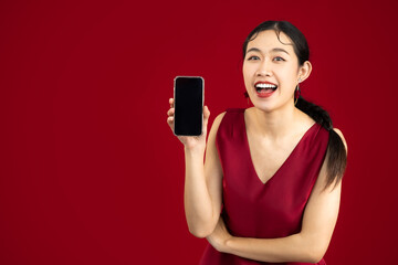Young beautiful asian woman wear elegant red dress holding and showing blank screen smartphone on red color background. - obrazy, fototapety, plakaty