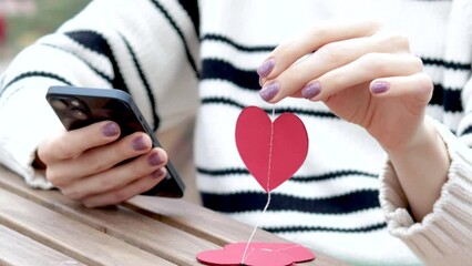 woman sitting in on table with paper hearts garland in one hand using smartphone with another,girl hugging red balloon heart shape.celebrate love valentine day coffee shop inside transparent balloon
