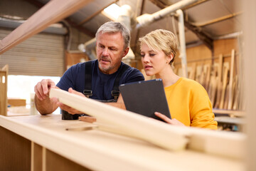 Female Apprentice With Digital Tablet Learning From Mature Male Carpenter In Furniture Workshop