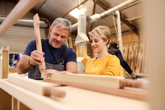 Female Apprentice Learning Skills From Mature Male Carpenter In Furniture Workshop