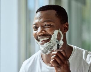 Face, shaving and razor with a black man grooming in the bathroom mirror of his home for beauty or skincare. Beard, shave and blade with a handsome male in the morning for his hair removal routine