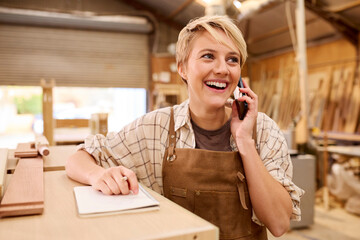 Female Apprentice Working As Carpenter In Furniture Workshop Making Phone Call