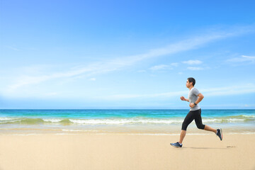 Asian man jogging  on tropical sandy beach with blue sea and clear sky background.