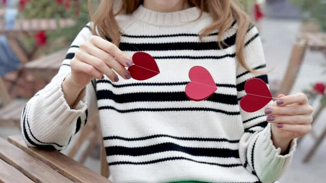 woman sitting in on table with paper hearts garland in one hand using smartphone with another,girl hugging red balloon heart shape.celebrate love valentine day coffee shop inside transparent balloon - Powered by Adobe