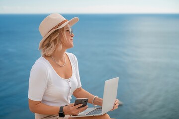 Freelance women sea working on the computer. Good looking middle aged woman typing on a laptop keyboard outdoors with a beautiful sea view. The concept of remote work.