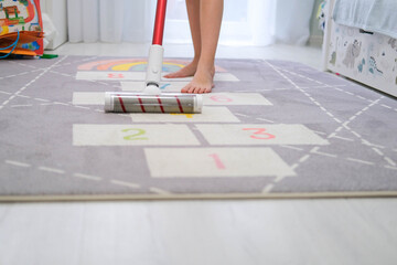 The child vacuums with a cordless vacuum cleaner in the nursery. Cleaning in the children's room,...