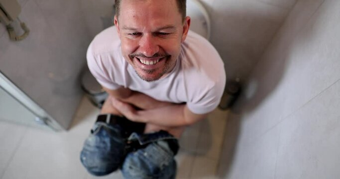 Happy smiling man is sitting in toilet in bathroom at home