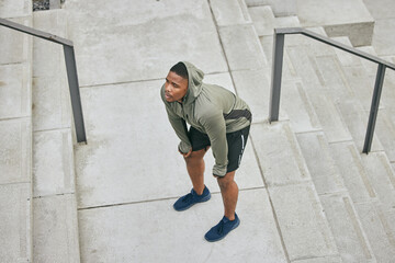Breathe, tired and sweating black man, athlete and fitness break on stairs of city workout. Top...