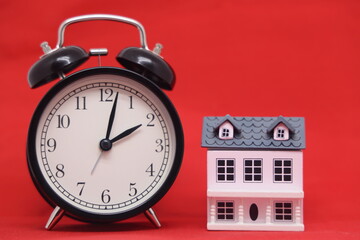 Toy house and black alarm clock isolated on red background. Mortgages and home purchases.
