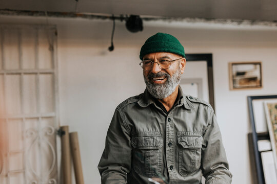Happy bearded craftsman wearing eyeglasses and knit hat in workshop