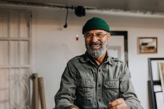 Portrait of cheerful male owner wearing knit hat and eyeglasses in workshop
