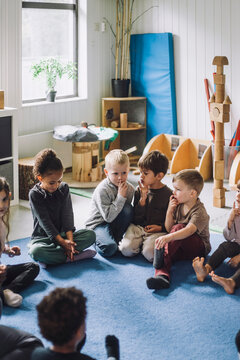 Multiracial boys and girls with fingers on lips sitting at kindergarten
