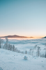 Fototapeta na wymiar View of sea of clouds colored in the soft orange-pink hue of the morning sun. Peaks of the mountains rising out of this impermeable curtain. Sense of immortality and bliss. Beskydy, Czech republic