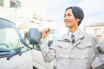 トラックの前でガッツポーズをする若い男性ドライバー