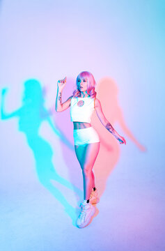 Young woman with pink hair dancing and having fun. Colored gel portraits with futuristic outfit