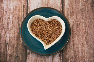small grains of natural brown buckwheat in a decorative plate in the form of a heart