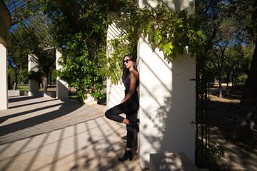 beautiful, brunette Spanish woman with black sunglasses. The woman is in the park lying on a park hill. The woman is serious and dressed in black clothes.