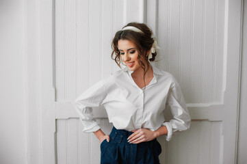 a sexy girl dressed in a white shirt and jeans poses indoors in front of a white door;