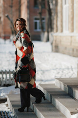 a sexy girl dressed in a long fur coat poses on the street; walks along the winter street holding a handbag