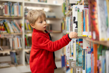 Adorable little boy, sitting in library, reading book and choosing what to lend, kid in book store.