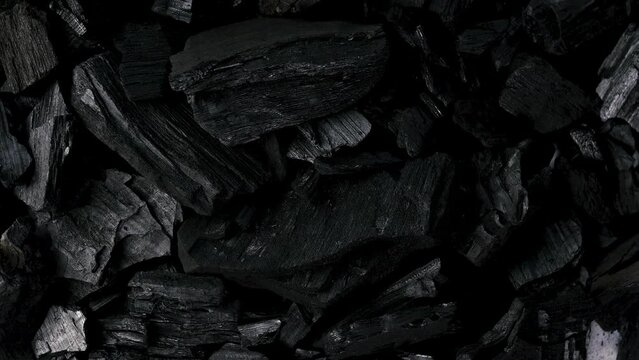 Black background of heap natural charcoal mineral used in industry and food preparation rotate.