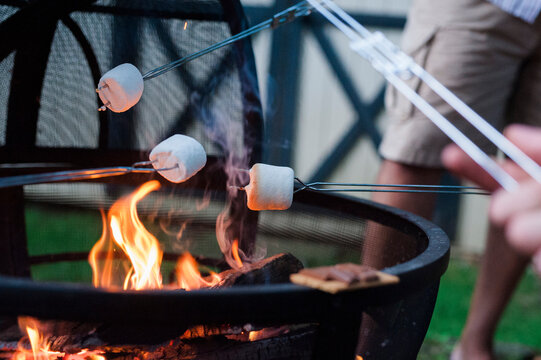 Midsection of man roasting marshmallow on campfire at yard