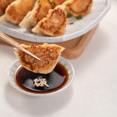 Pan-fried gyoza dumpling jiaozi in a plate with soy sauce on white table background.