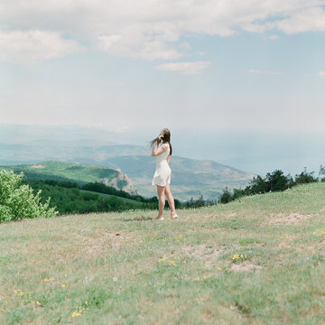 A woman in a white dress is standing on a cliff near the sea