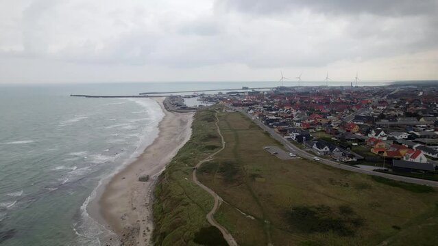 Over flight of Hirtshal village beach coastline on cloudy day with wind turbines
